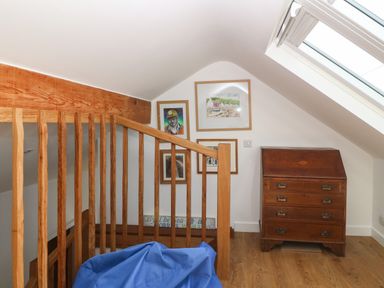 A wooden staircase railing with framed pictures on a white wall and a wooden chest of drawers under a skylight at Fron Olau in Nefyn