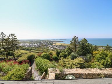 A garden with shrubs and trees overlooking a town and sea at Fron Olau in Nefyn