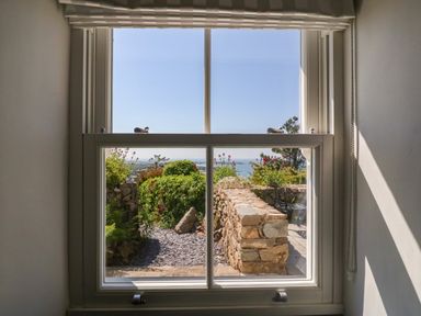 A window showing a garden path with stone walls and a view of the sea at Fron Olau in Nefyn