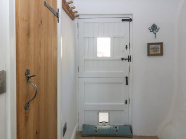 A white wooden stable door with a small window and a pet door at the bottom with a draft stopper and a wooden coat rack on the wall at Fron Olau in Nefyn