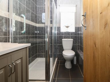 A bathroom with a shower, toilet, cabinet, and window at Fron Olau in Nefyn