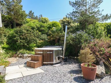 An outdoor hot tub with wooden steps surrounded by gravel and plants at Fron Olau in Nefyn