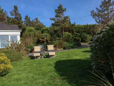 A garden with two chairs and a small table near a house surrounded by trees and bushes at Fron Olau in Nefyn