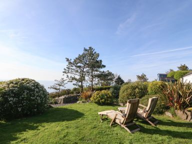 A garden area with grass wooden lounge chairs and various bushes at Fron Olau in Nefyn