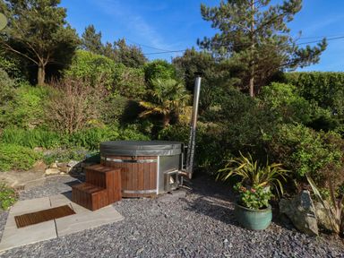 An outdoor hot tub with wooden steps surrounded by gravel and greenery at Fron Olau in Nefyn