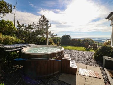 An outdoor area with a wooden hot tub garden chairs and a view of the sea at Fron Olau in Nefyn