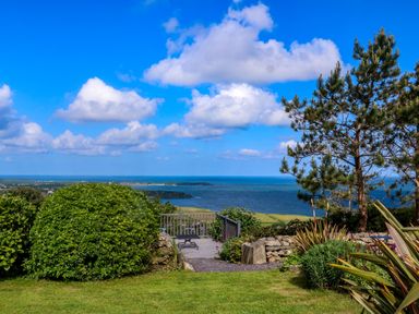 A garden with bushes trees and a bench overlooking the sea at Fron Olau in Nefyn