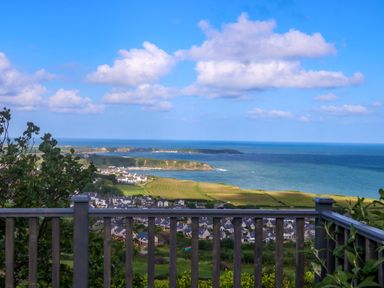 A coastal view from a wooden balcony overlooking houses fields and the sea at Fron Olau in Nefyn