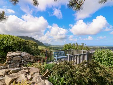 A garden area with a wooden bench and stone wall overlooking hills and fields at Fron Olau in Nefyn