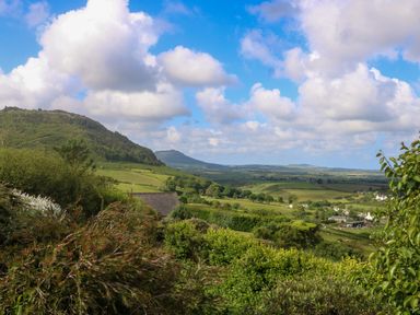 A rural landscape with green hills trees and houses under a blue sky with clouds at Fron Olau in Nefyn