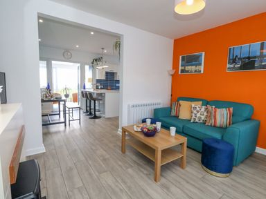 A living room with teal sofa and wooden coffee table next to an open kitchen with bar stools at Lagoon View in Wyke