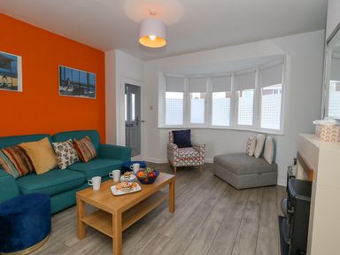 A living room with a teal sofa and wooden coffee table with snacks and drinks a patterned armchair and grey chaise lounge by bay windows at Lagoon View in Wyke