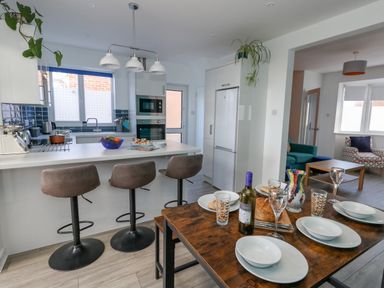 A kitchen with stools at a counter and a dining table set with plates and glasses at Lagoon View in Wyke