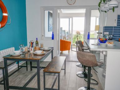 A dining area with a wooden table set with dishes and glasses next to a kitchen counter with bar stools and a view of an outdoor sitting area at Lagoon View in Wyke