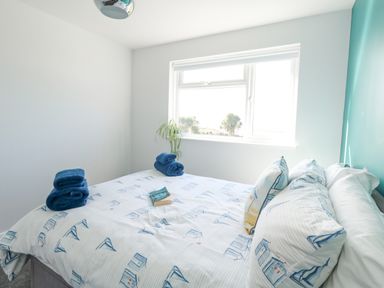A bedroom with a bed with blue patterned bedding and folded towels by a window with a plant at Lagoon View in Wyke