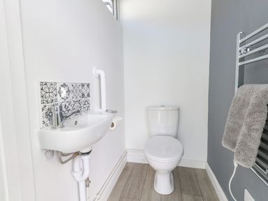 A small bathroom with a white toilet, a wall-mounted sink with patterned tiles behind it, and a heated towel rail with a gray towel at Lagoon View in Wyke