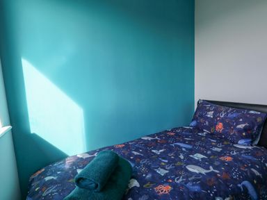A bed with ocean-themed bedding and folded towels on top against a turquoise and white wall at Lagoon View in Wyke