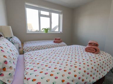A bedroom with two single beds covered in fruit patterned bedding and pink towels on the beds at Lagoon View in Wyke