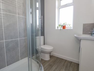 A bathroom with a shower enclosure toilet sink and a window with a plant on the sill at Lagoon View in Wyke