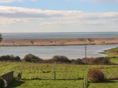 A grassy field with bushes and a fence overlooking a body of water and a sandy strip with the sea in the background at Lagoon View in Wyke