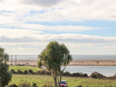 A coastal landscape with palm trees a red car green grass shrubs water and cloudy sky at Lagoon View in Wyke