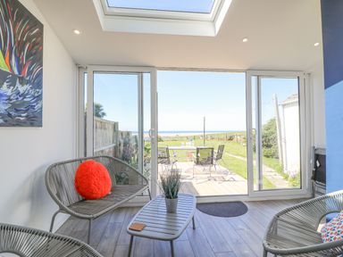 A sunroom with wicker furniture and a red cushion facing glass doors overlooking a patio and grassy yard at Lagoon View in Wyke