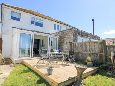 A backyard patio with glass table and chairs next to a house with sliding glass doors at Lagoon View in Wyke