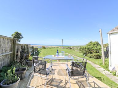 An outdoor patio with a table and four chairs overlooking a grassy backyard and the sea at Lagoon View in Wyke