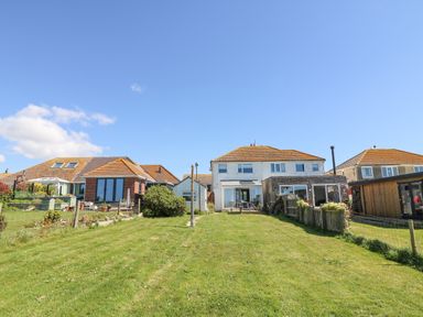 A backyard with a lawn and three houses under a blue sky at Lagoon View in Wyke