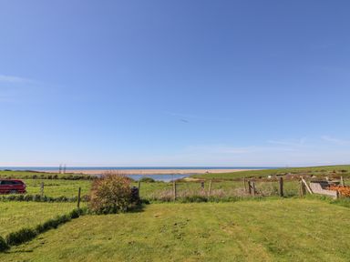 A grassy field with a bush and a distant view of the sea under a clear sky at Lagoon View in Wyke