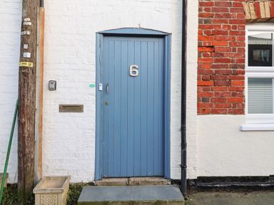 A blue door with number 6 on a white and red brick wall next to a window at Tuckaway Cottage in Aldeburgh