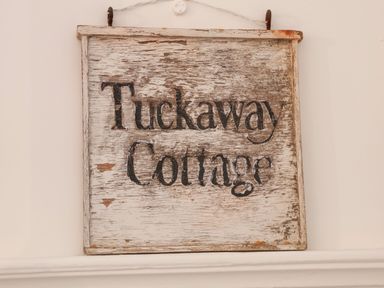 A weathered wooden sign with the words Tuckaway Cottage on a white wall at Tuckaway Cottage in Aldeburgh