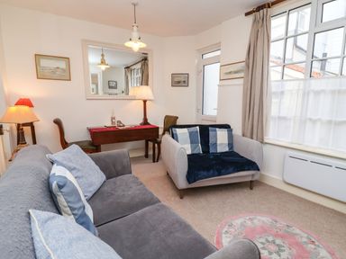 A living room with two sofas a desk with a lamp and chairs a large window and a round rug at Tuckaway Cottage in Aldeburgh