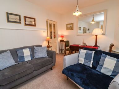 A living room with two sofas with cushions a small table with a lamp a wooden chair and a large mirror at Tuckaway Cottage in Aldeburgh