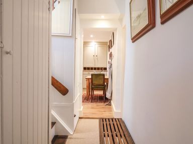 A hallway with wooden bench and staircase leading to a dining area with table and chairs at Tuckaway Cottage in Aldeburgh