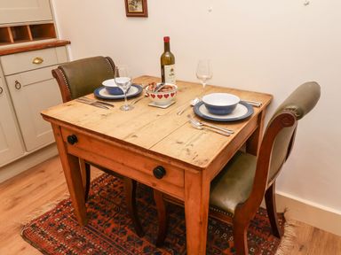 A wooden dining table with two chairs set with plates bowls wine glasses cutlery and a bottle at Tuckaway Cottage in Aldeburgh