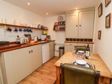 A kitchen with wooden countertops cabinets a dining table with chairs and dishes at Tuckaway Cottage in Aldeburgh