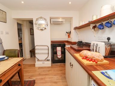 A kitchen with wooden countertops a stove a toaster bread and tomatoes on a cutting board and a dining table at Tuckaway Cottage in Aldeburgh