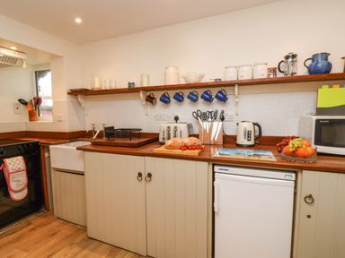 A kitchen countertop with bread and cherry tomatoes chopping board knives hanging blue mugs toaster kettle microwave and fruit bowl at Tuckaway Cottage in Aldeburgh