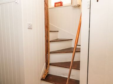 A narrow wooden staircase with dark brown steps and white panel walls and a rope hanging on the left side at Tuckaway Cottage in Aldeburgh