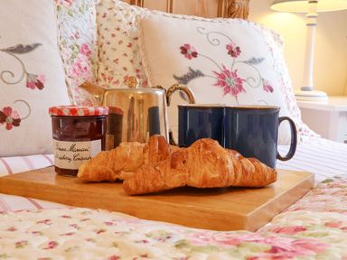 A wooden tray with croissants jam teapot and two blue mugs on a floral bed at Tuckaway Cottage in Aldeburgh