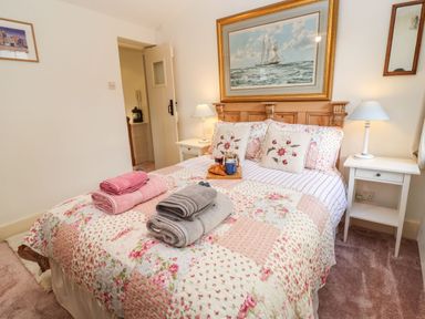 A bedroom with a floral quilt on the bed towels on the bed and a painting of a sailing ship above the headboard at Tuckaway Cottage in Aldeburgh