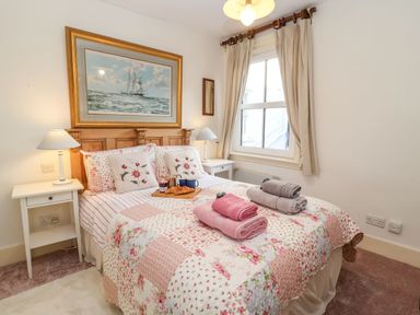 A bedroom with a double bed covered with floral quilt and towels on the bed beside bedside tables with lamps and a window at Tuckaway Cottage in Aldeburgh