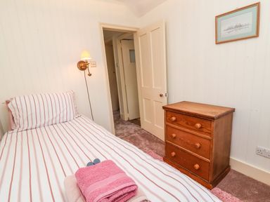 A bedroom with a single bed with striped bedding a wooden chest of drawers and a wall lamp at Tuckaway Cottage in Aldeburgh