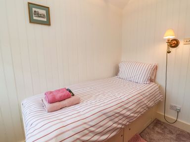 A small bedroom with a single bed striped bedding towels on the bed a wall lamp and a framed picture at Tuckaway Cottage in Aldeburgh