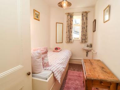 A small bedroom with a single bed next to a window a wooden desk and a small corner sink at Tuckaway Cottage in Aldeburgh