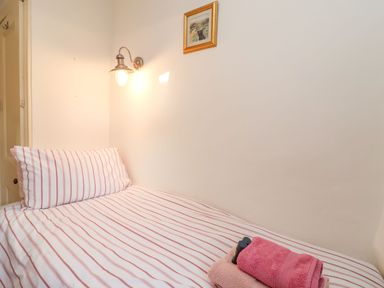 A single bed with striped bedding towels on top and a wall lamp above at Tuckaway Cottage Aldeburgh