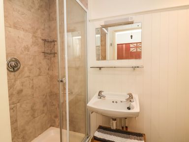 A bathroom with a shower enclosure a sink a mirror and a striped rug at Tuckaway Cottage in Aldeburgh