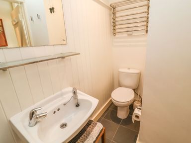 A small bathroom with a white sink, toilet, mirror, and towel rack at Tuckaway Cottage in Aldeburgh