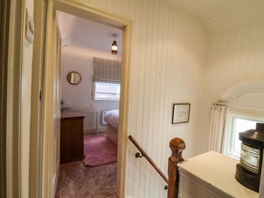 A hallway with wooden panel walls leading to a bedroom with a bed and a dresser at Tuckaway Cottage in Aldeburgh